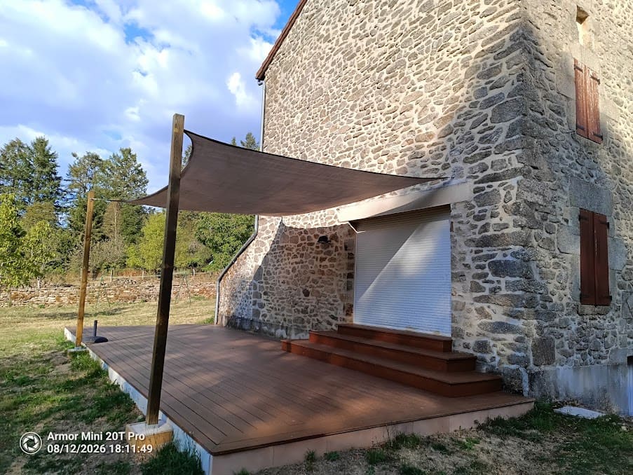Terrasse en bois et voile d'ombrage le long d'une maison en pierre